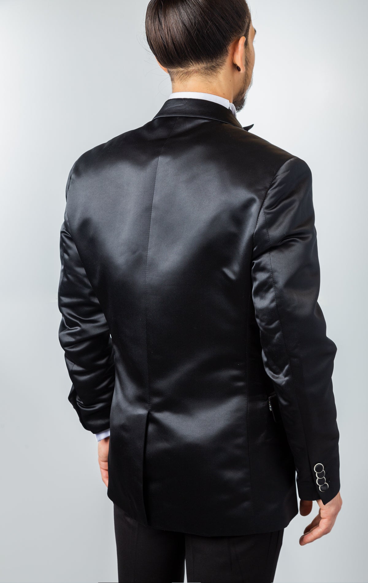 Black, one-button tuxedo jacket with a slim fit. The jacket features a shiny black fabric, rhinestone embellishments on the collar, a pocket square, and button cuffs. The jacket is made from a medium-lightweight fabric.