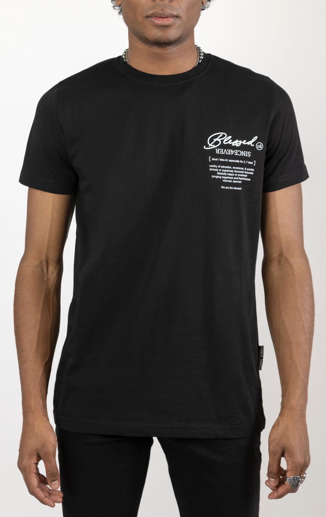 Men's regular fit t-shirt in black. The shirt features a slightly elongated sleeve, a fitted neckline, and a straight body. It has a "Forever a Saint, Never a Snake" digital print on the back with 3D "blessed" embroidery. Made from 100% cotton. A "blessed" slogan is printed on the inner neck binding and a woven side seam tab with "blessed" is also included. The front features a "blessed" with a strikethrough design and the back neck features a signature "blessed" script print.
