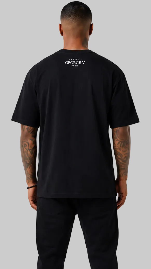 A man viewed from the back wearing a black short-sleeve t-shirt with a small white 'GEORGE V PARIS' logo printed on the upper back, paired with black pants, against a solid gray background.