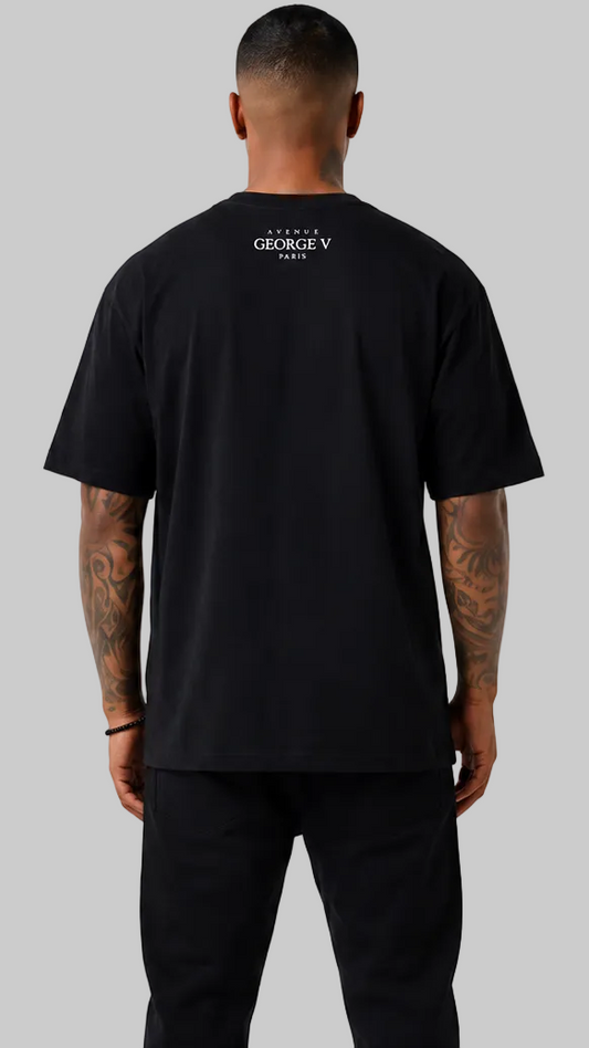 A man viewed from the back wearing a black short-sleeve t-shirt with a small white 'GEORGE V PARIS' logo printed on the upper back, paired with black pants, against a solid gray background.