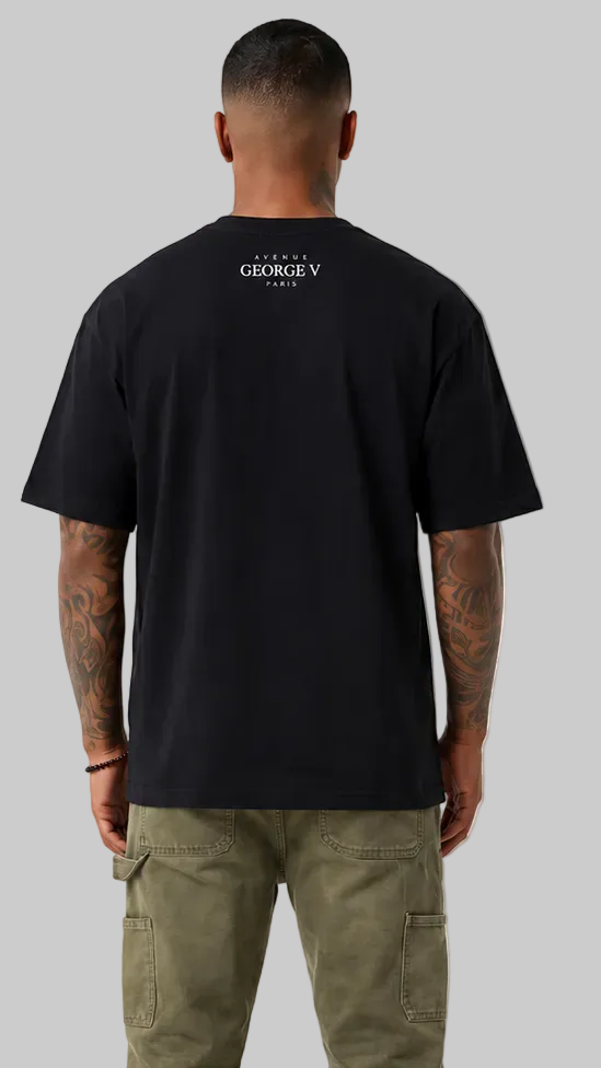 A man viewed from the back wearing a black short-sleeve t-shirt with a small white 'GEORGE V PARIS' logo printed on the upper back, paired with olive green cargo pants, against a solid gray background.