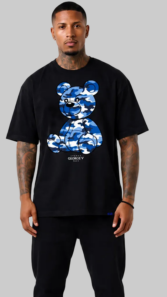 A man wearing a black t-shirt with a blue camouflage bear graphic on the front, standing against a solid gray background.