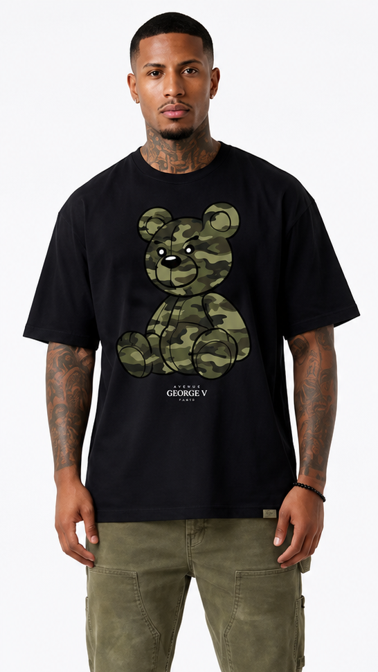 A man modeling a black short-sleeve t-shirt from the front, paired with olive cargo pants and sneakers. The front of the t-shirt features a green camouflage graphic of a teddy bear 