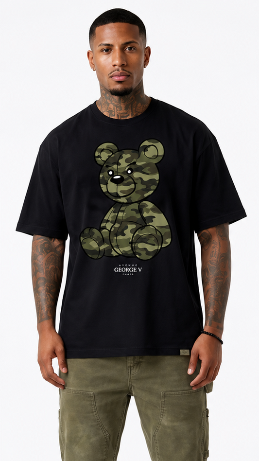 A man modeling a black short-sleeve t-shirt from the front, paired with olive cargo pants and sneakers. The front of the t-shirt features a green camouflage graphic of a teddy bear 