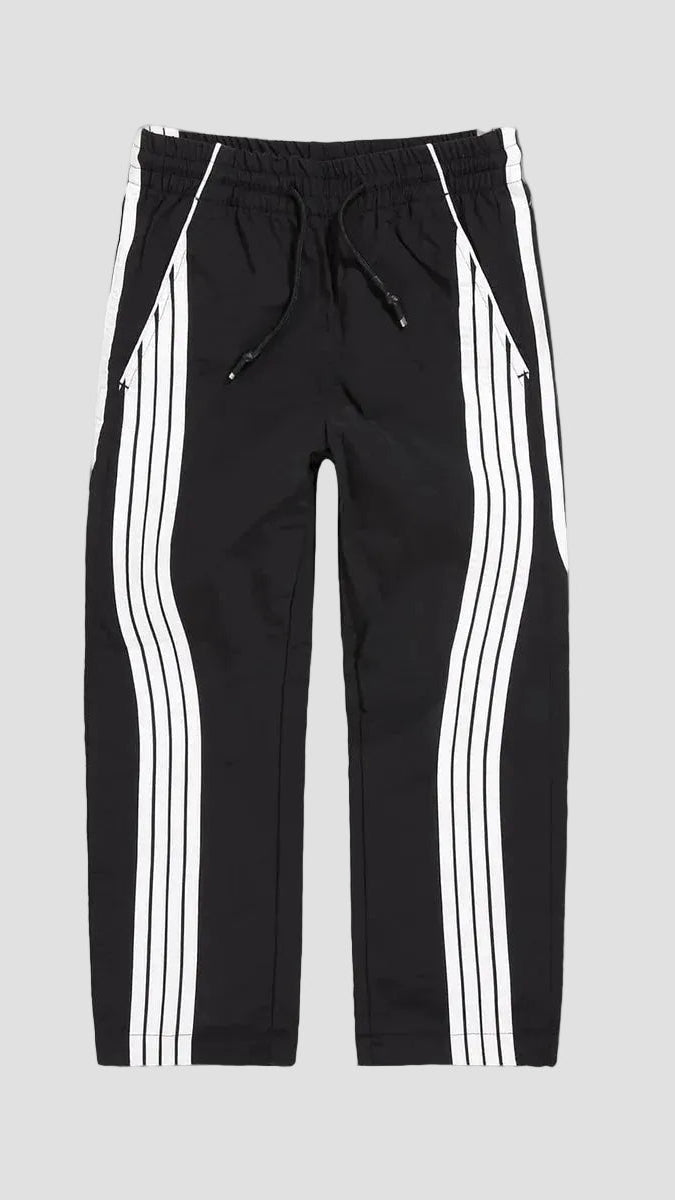 Black track pants with white double stripes down the sides, featuring an elastic waistband and drawstring, shown against a solid gray background.