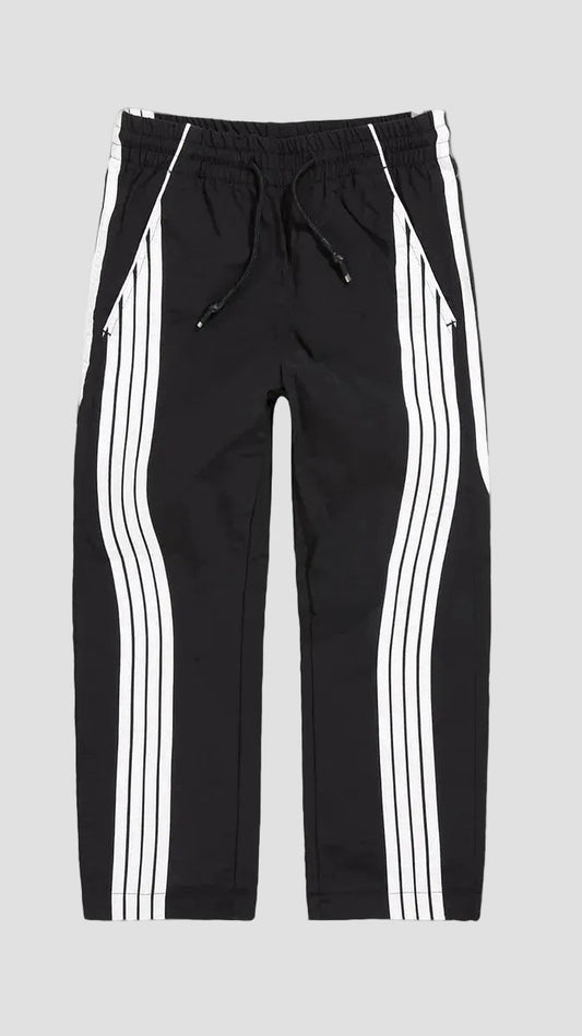 Black track pants with white double stripes down the sides, featuring an elastic waistband and drawstring, shown against a solid gray background.