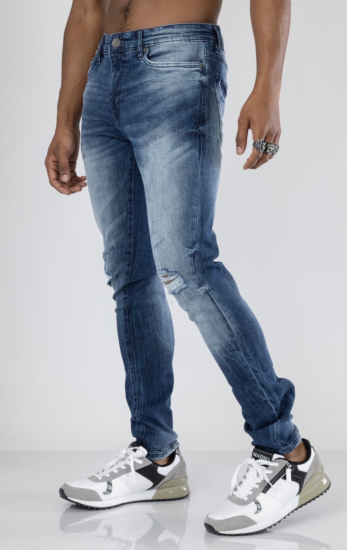 Men's ripped and distressed denim pants in a variety of washes. The pants feature a regular rise, tapered fit from the knee down, open rips at the knees, unique distressing details, and are made from 98% cotton with 2% lycra for stretch