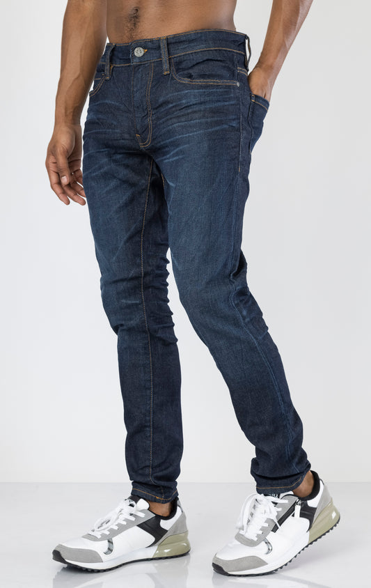 Men's Sean Slim Taper jeans in dark indigo. The jeans feature a regular rise waist, a comfortable fit from waist to thigh, a slim taper from knee to ankle, 3D baked wrinkles for texture, a raw denim look, and are made from a super stretch fabric blend (35% Cotton, 30% Polyester, 34% Tencel and 1% Elastane).