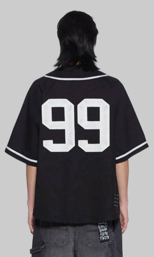 A person shown from the back wearing an oversized black baseball-style jersey with large white '99' lettering on the back and white trim on the collar and sleeve cuffs, paired with dark gray jeans against a plain white background.