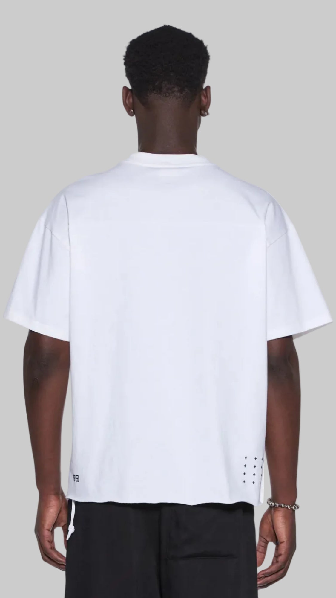 A man viewed from the back wearing a white short-sleeve t-shirt and black pants, set against a plain white background.