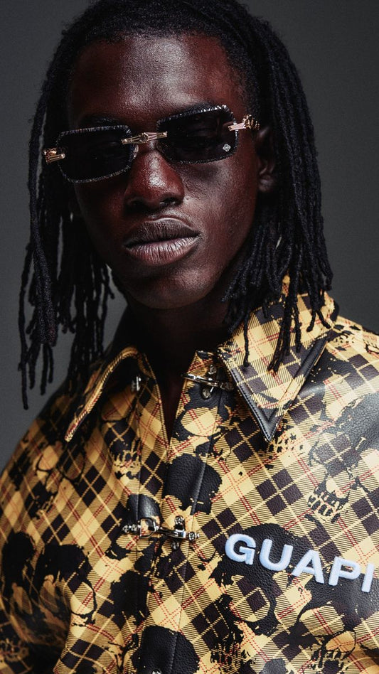 Person wearing a patterned shirt with 'GUAPI' branding against a dark background