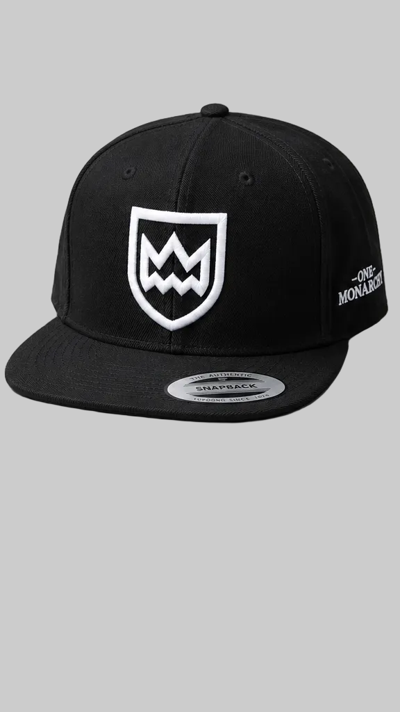 A black flat-brim snapback cap featuring a white embroidered shield logo on the front and 'ONE MONARCHY' text on the side, shown against a solid gray background.