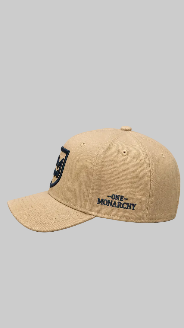 A khaki baseball cap with embroidered dark colored logos on the front and side, reading 'ONE MONARCHY', shown against a solid gray background.