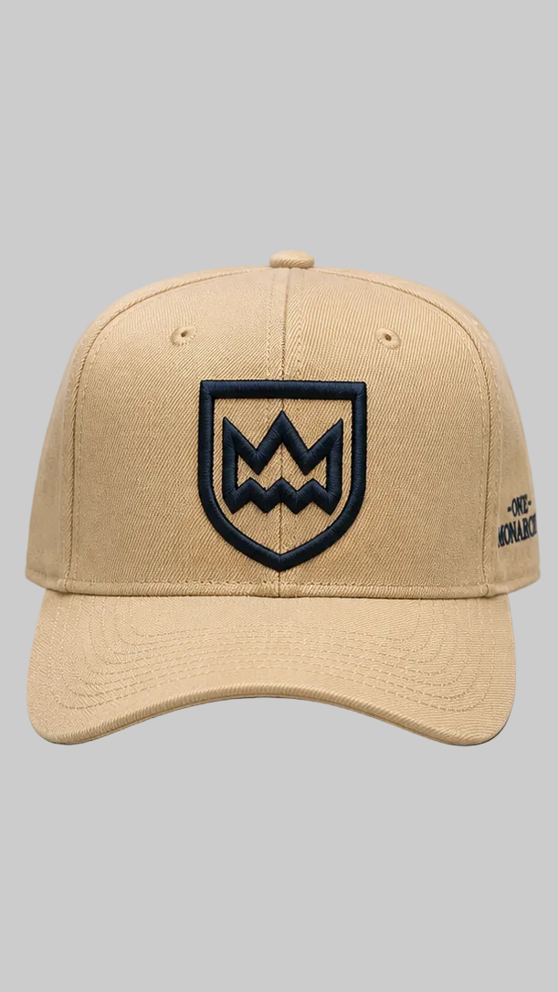 A beige baseball cap featuring a dark Colored embroidered shield logo on the front and a small side tag, shown against a solid gray background.