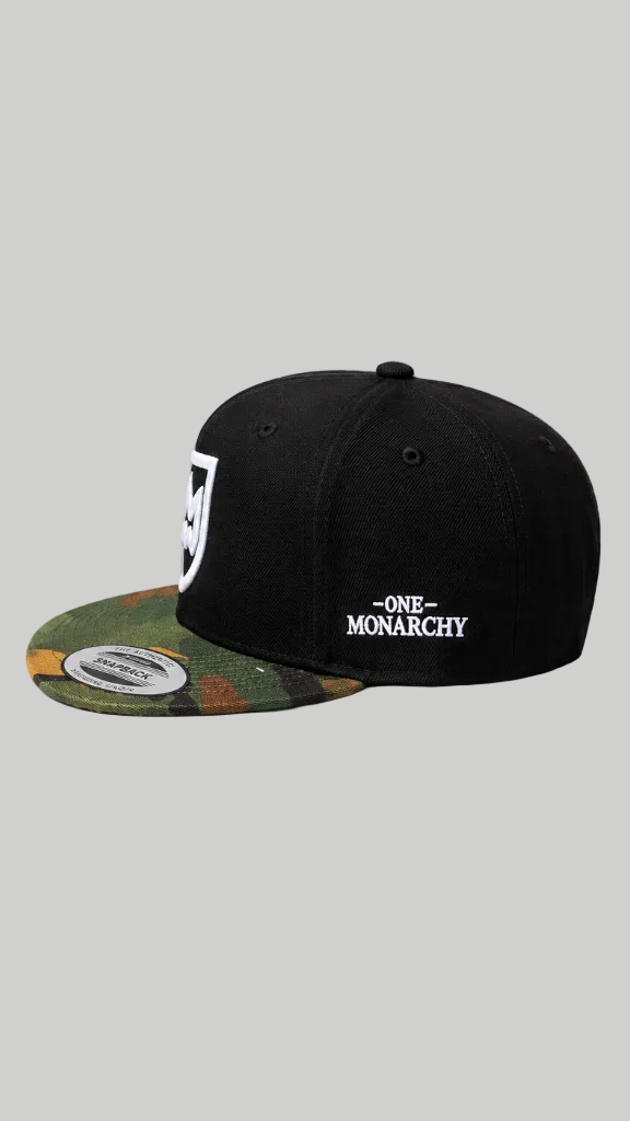 A black snapback cap with a camouflage-patterned brim and white embroidered text reading 'ONE MONARCHY' on the front, shown against a solid gray background.