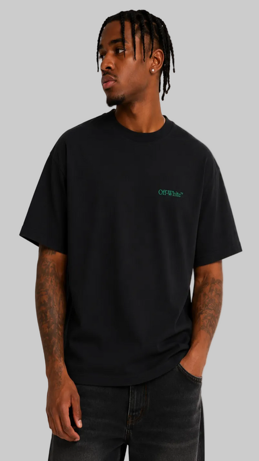 A man wearing a black crewneck t-shirt with a small green 'OFF-WALL' logo on the left chest, paired with dark jeans, photographed against a light gray studio background.
