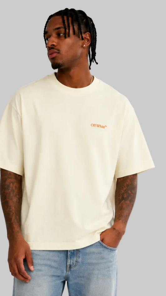 A man wearing a cream-colored oversized t-shirt with a small orange 'off-White' logo on the left chest, paired with light blue jeans