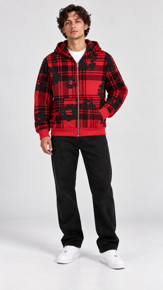 A man modeling a red and black plaid zip-up hoodie with a black graphic print, paired with black sweatpants and white sneakers, against a light gray studio background.