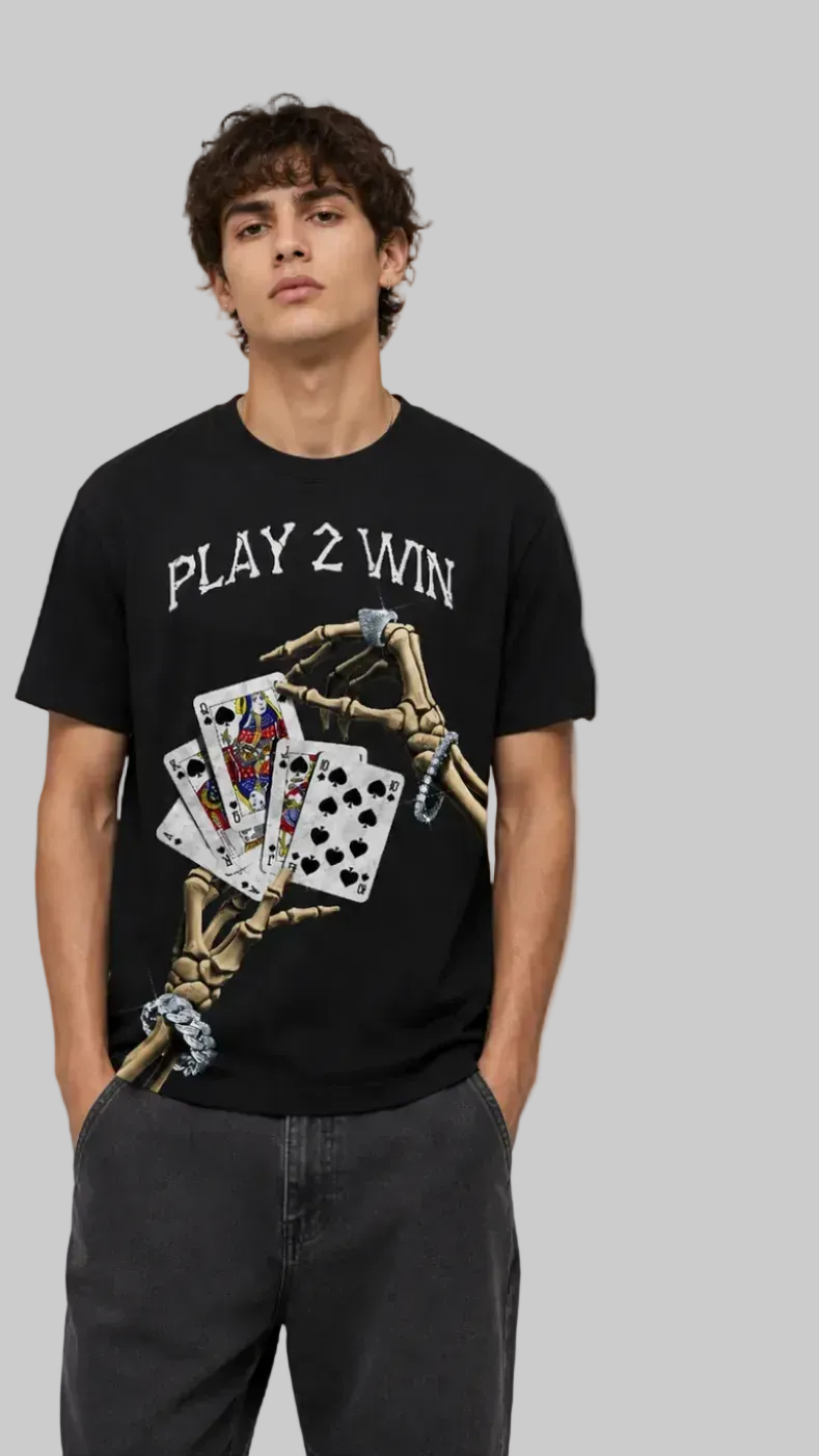 A man modeling a black graphic T-shirt shown front against a light gray studio background. The front features the text 'PLAY 2 WIN' above a skeletal hand holding playing cards
