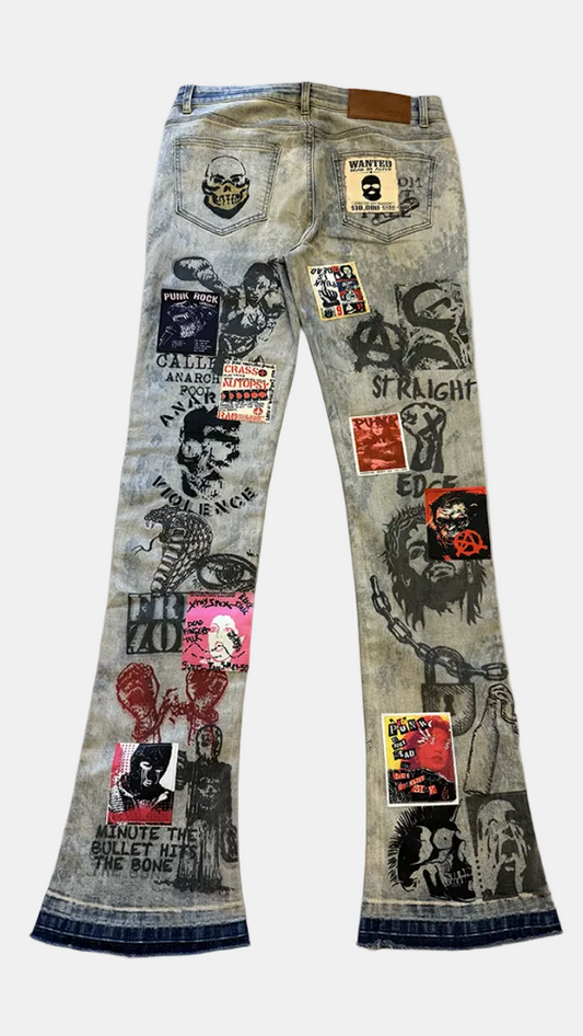 Distressed light-wash blue jeans with extensive black graphic prints, patches, and stickers, featuring a flared leg and denim cuffs.