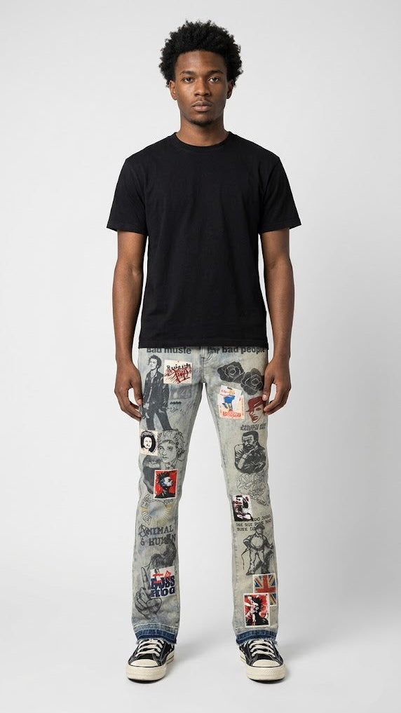 A man stands against a light gray studio background wearing a plain black short-sleeve T-shirt, light gray distressed jeans covered with many small graphic patches, and black-and-white sneakers.