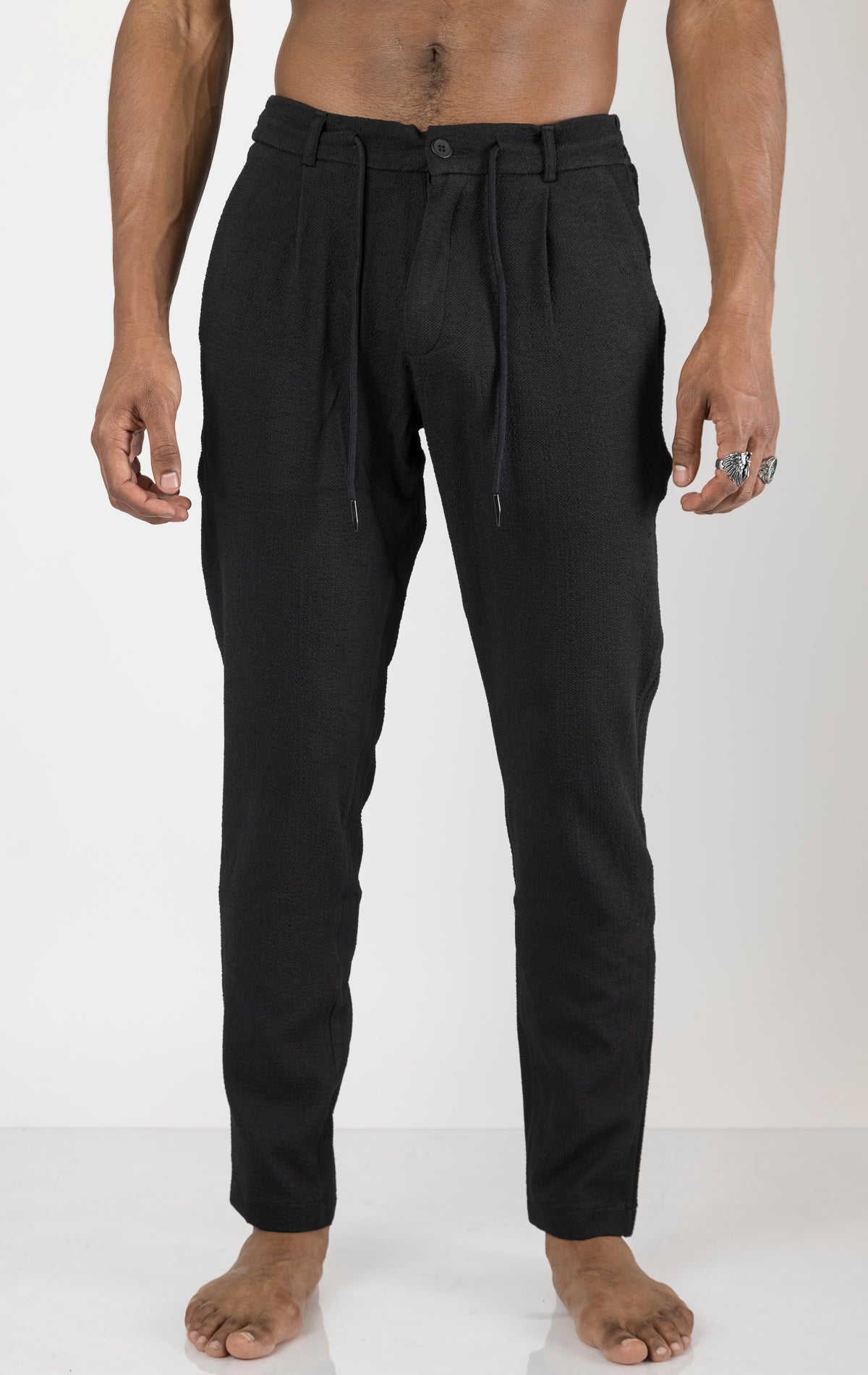 Men's front pleated waffle pants in black. The pants are made from a textured waffle fabric (95% cotton, 5% elastane) and feature a relaxed fit, front pleats, and a comfortable elastic waistband.