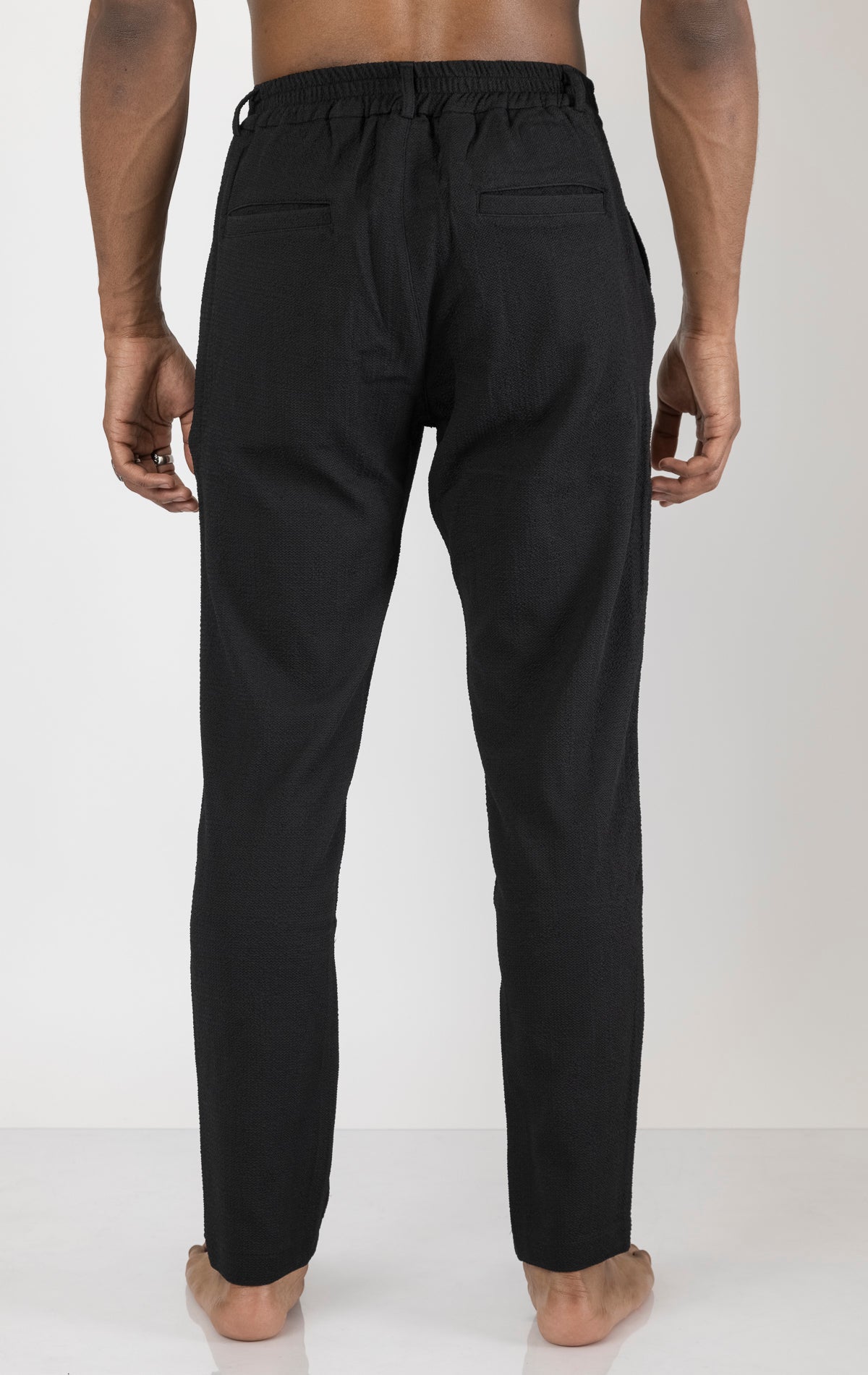 Men's front pleated waffle pants in black. The pants are made from a textured waffle fabric (95% cotton, 5% elastane) and feature a relaxed fit, front pleats, and a comfortable elastic waistband.