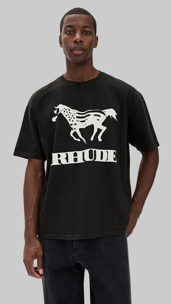 A man wearing a black short-sleeve t-shirt with a white graphic of a running horse and the word 'RHUDE' printed across the chest, against a light gray background.