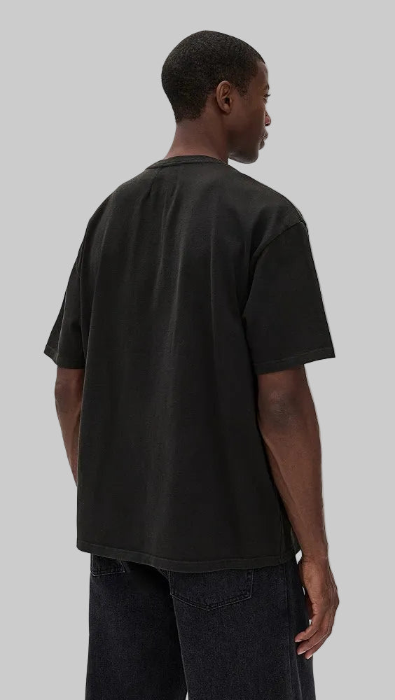 A man wearing a black oversized short-sleeve t-shirt, shown from the back against a plain light gray studio background.