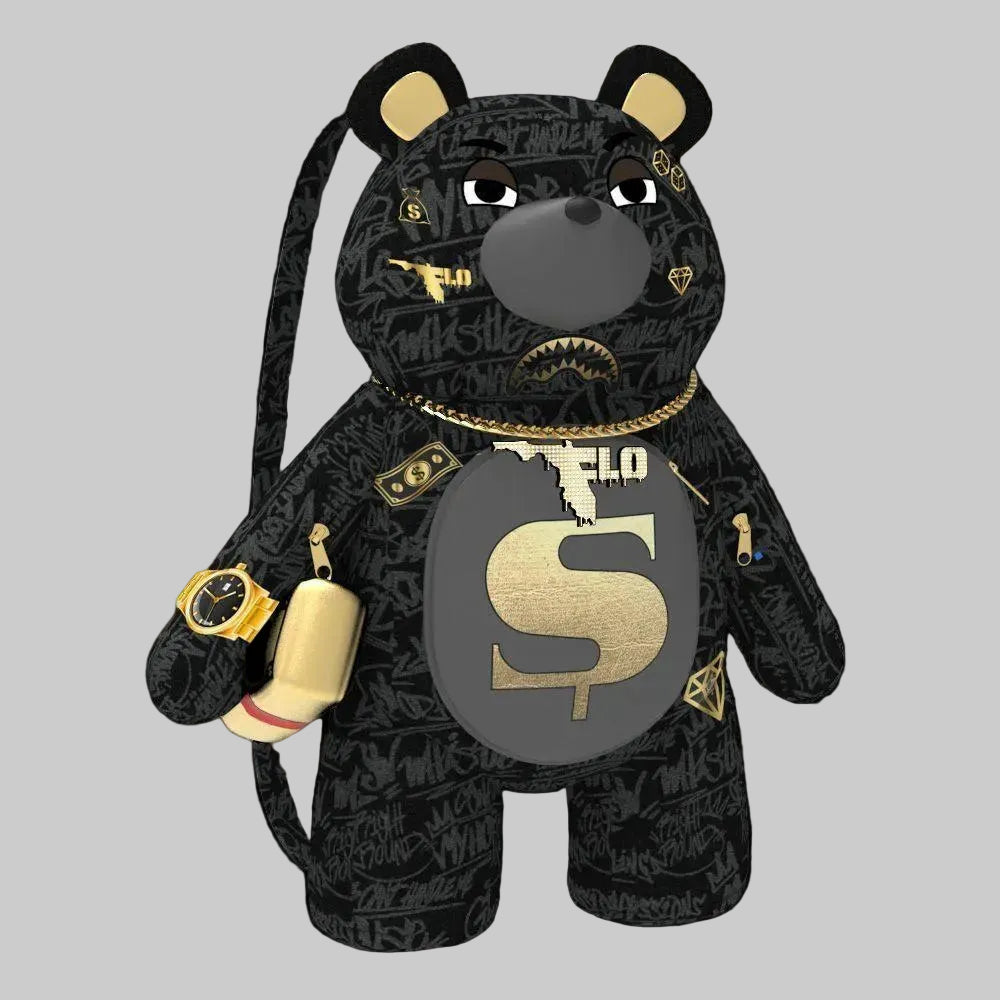 A black plush bear accessory with a gold and gray graffiti-style print, featuring a large gold 'S' on its belly, a gold chain necklace, a gold watch, and a small gold bottle, shown on a plain white background.