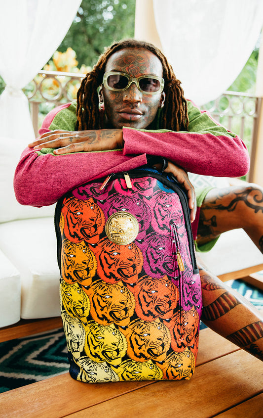 Sprayground Tigers on My Mind Backpack. The backpack is made from durable faux leather (100% PVC) and features a gold metal plated tiger emblem, a front zipper pocket, side pockets, a zippered stash pocket, a separate velour sunglass compartment, ergonomic mesh back padding, adjustable straps, and a slide through back sleeve that connects to carry-on luggage. The interior includes a separate velour laptop compartment and a mesh organizer pocket.  pen_spark     tune  share   more_vert