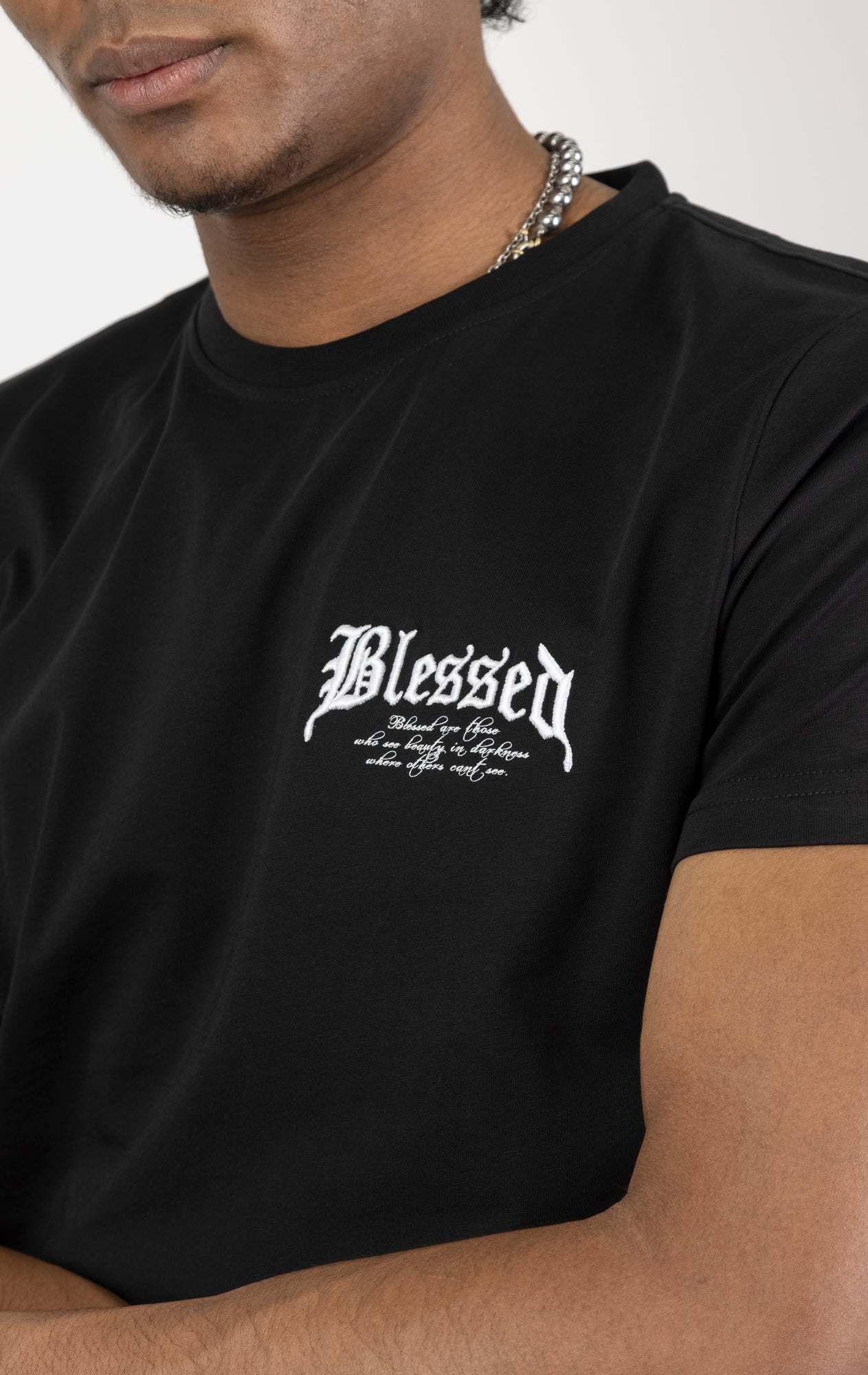Men's regular fit t-shirt in black. The shirt features a slightly elongated sleeve, a fitted neckline, and a straight body. It has "Blessed with Beauty" printed on the front and back with 3D embroidery. Made from 100% cotton jersey (190gsm). A "blessed" slogan is printed on the inner neck binding and a woven side seam tab with "blessed" is also included.