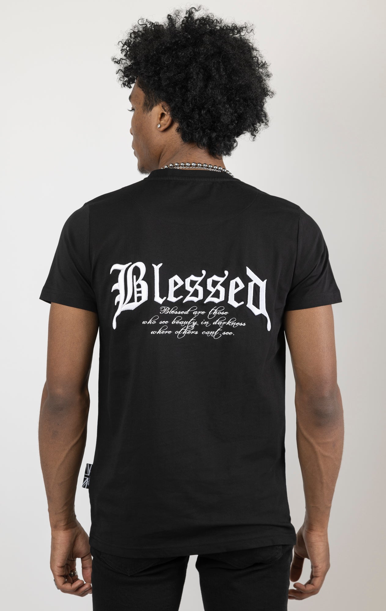 Men's regular fit t-shirt in black. The shirt features a slightly elongated sleeve, a fitted neckline, and a straight body. It has "Blessed with Beauty" printed on the front and back with 3D embroidery. Made from 100% cotton jersey (190gsm). A "blessed" slogan is printed on the inner neck binding and a woven side seam tab with "blessed" is also included.