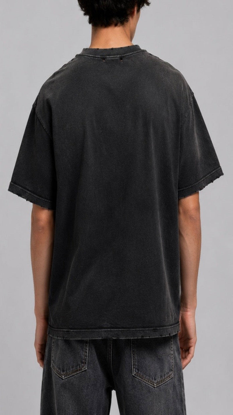 A person shown from the back wearing an oversized faded black t-shirt and dark gray jeans against a solid gray studio background.