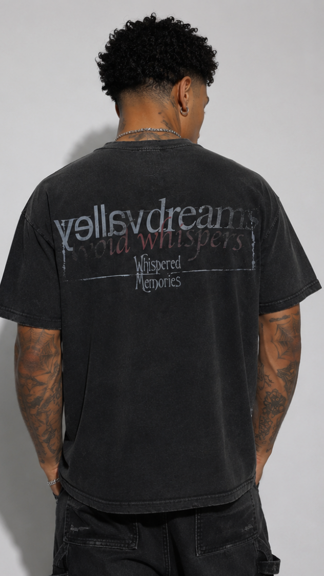 A man viewed from behind wearing a washed black t-shirt with a distressed graphic on the back that reads 'valley dreams' and 'Whispered Memories'.