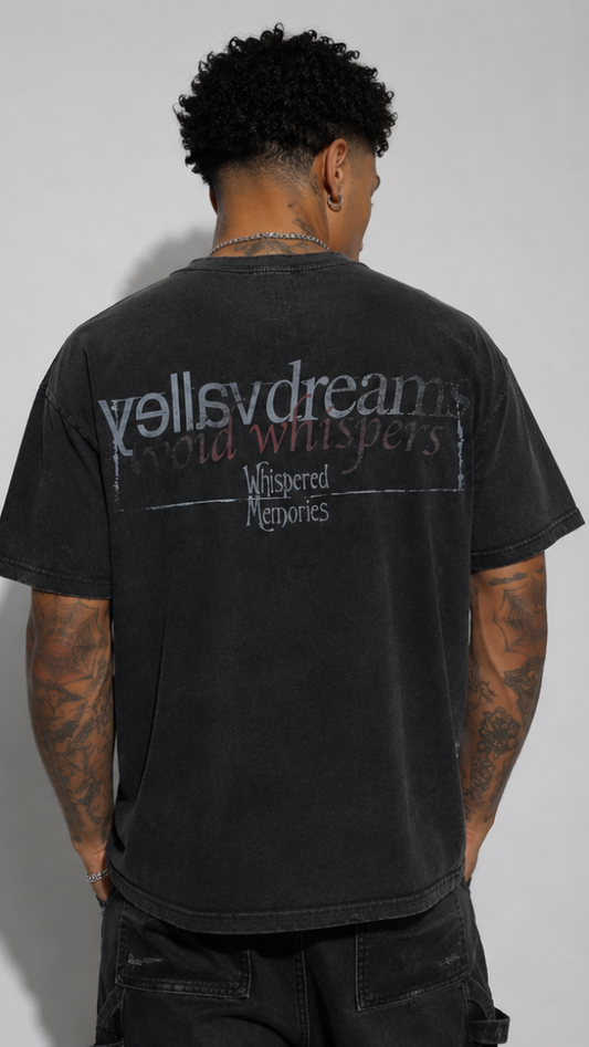 A man viewed from behind wearing a washed black t-shirt with a distressed graphic on the back that reads 'valley dreams' and 'Whispered Memories'.