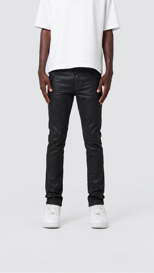 A model from the chest down wearing slim-fit black jeans, a white t-shirt, and white sneakers, standing against a light gray studio background.