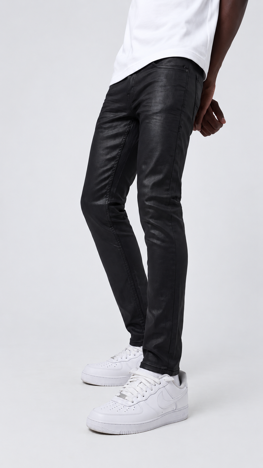 A person wearing slim black leather-look jeans with a white t-shirt and white sneakers, shown from the waist down against a light gray studio background.
