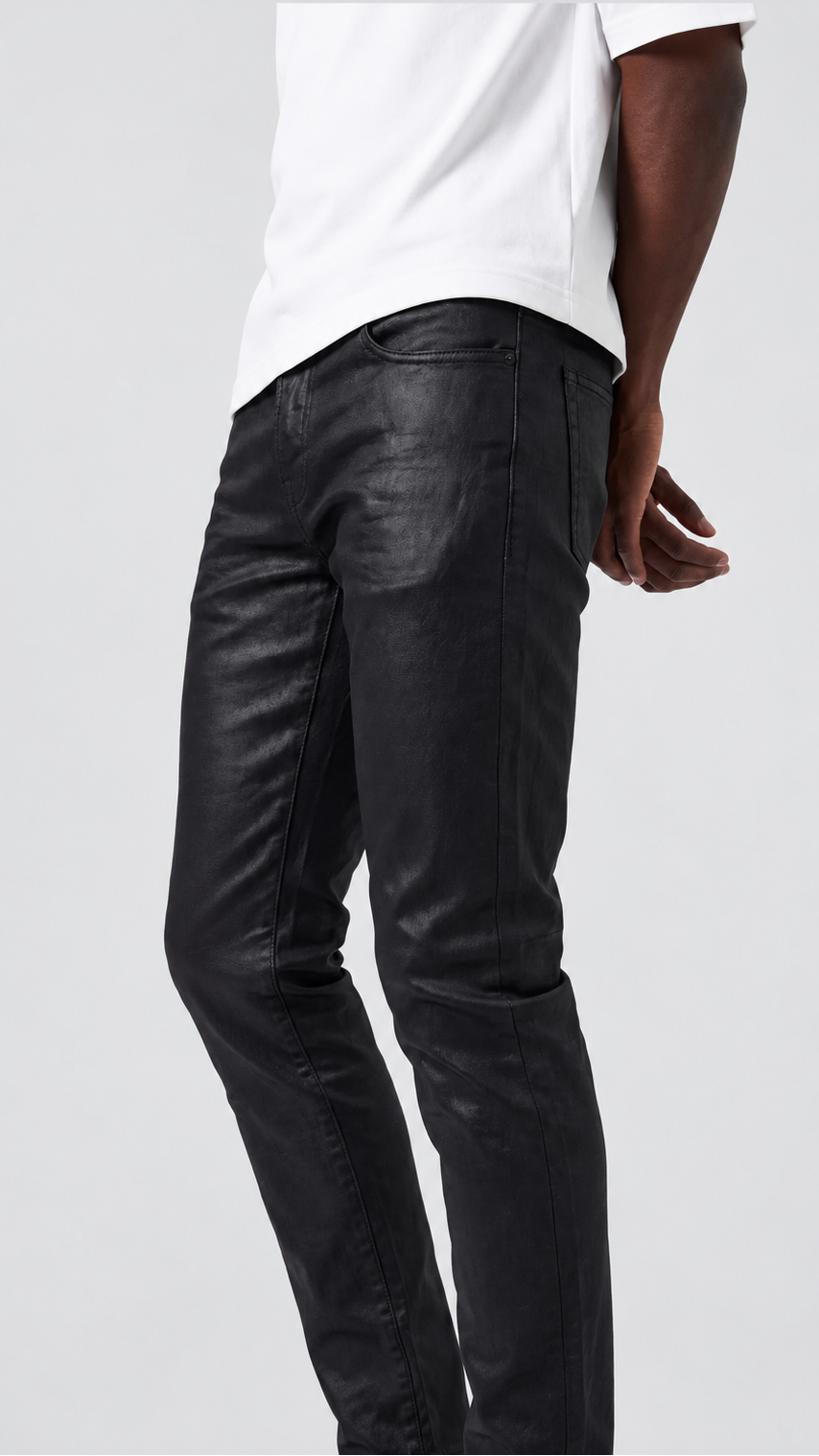 A person wearing slim black leather-look jeans and a white T-shirt, shown from the back against a light gray studio background.