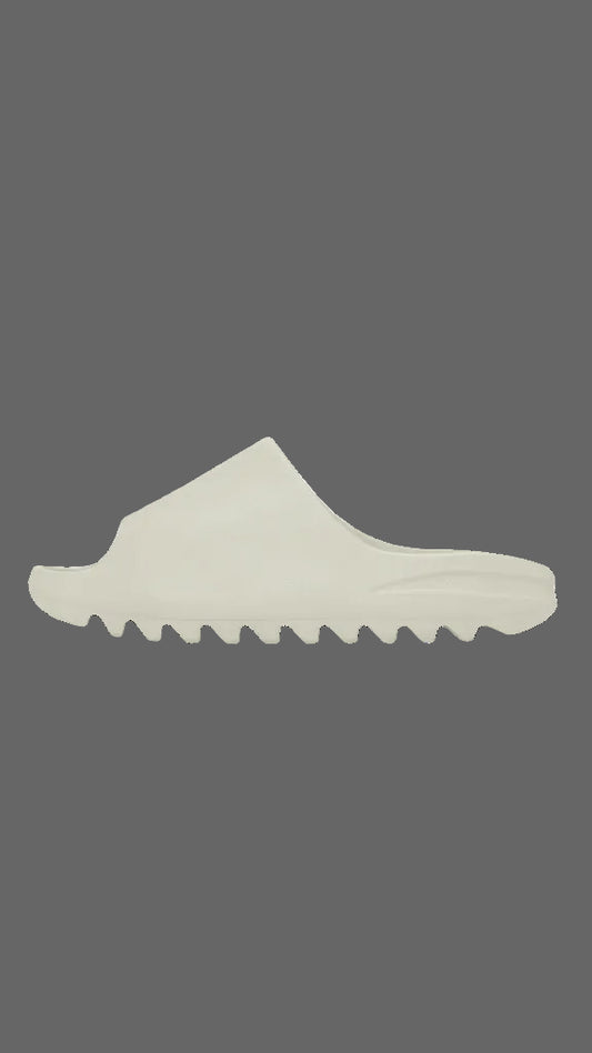 A single off-white slip-on shoe with a wavy, sculpted sole, shown in a side profile against a solid dark gray background.